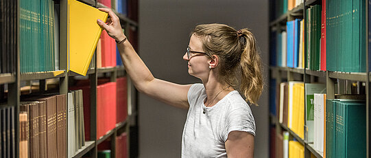 Studierende in der Bibliothek greift nach Buch im Regal