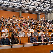 Hörsaal mit voll belegten Sitzen und stehenden Personen.
