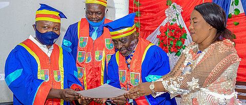 Der Rektor, Prof. J.-B. Muhigwa (zweiter von rechts), zusammen mit der Vertreterin des Gouverneurs, E. Camunani, und dem Vizerektor, Prof. V. Nshombo überreichen stellvertretend Dr. S. Muyisa (ganz links) die Ehrenpromotionsurkunde.