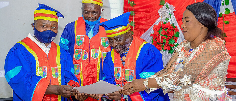 Der Rektor, Prof. J.-B. Muhigwa (zweiter von rechts), zusammen mit der Vertreterin des Gouverneurs, E. Camunani, und dem Vizerektor, Prof. V. Nshombo überreichen stellvertretend Dr. S. Muyisa (ganz links) die Ehrenpromotionsurkunde.