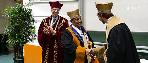 Dekan Holger Helten und Präsident Paul Pauli gratulieren Professor Jarugu Narasimha Moorthy zum Erhalt der Ehrendoktorwürde.